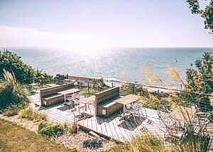 Deck overlooking the sea with tables and chairs, surrounded by greenery.